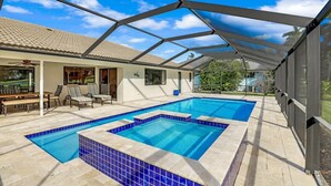A covered swimming pool area with two pools, a patio with seating, and a view of the surrounding landscape. - 216 Shadowridge Court (Marco Island)