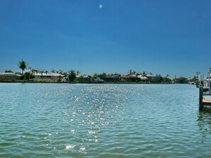A waterfront view with a dock extending into calm water, surrounded by residential buildings and palm trees. - 438 North Barfield Drive (Marco Island)