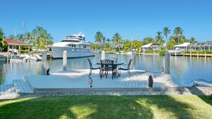 A marina with a yacht docked, a wooden deck with a table and chairs, and palm trees in the background. - 848 Buttonwood Court (Marco Island)