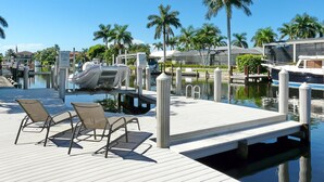 A marina with docked boats, a wooden deck with lounge chairs, and palm trees in the background. - 848 Buttonwood Court (Marco Island)