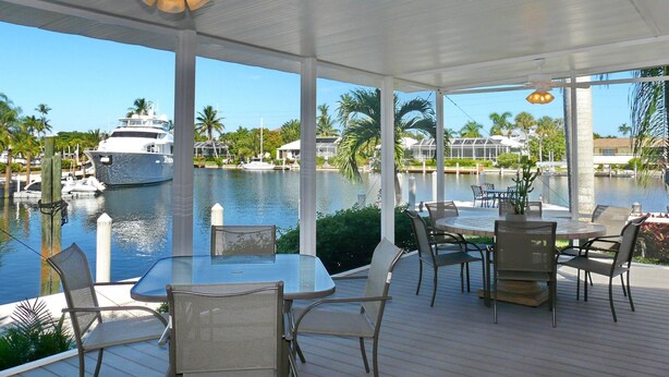 A covered outdoor area with a table and chairs, a ceiling fan, and a view of a marina with boats and palm trees. - 848 Buttonwood Court (Marco Island)