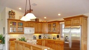 A modern kitchen with wooden cabinets, a stainless steel refrigerator, and a central island. - 848 Buttonwood Court (Marco Island)