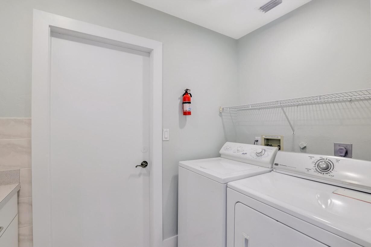 A laundry room with a white door, a fire extinguisher on the wall, and two stacked washing machines.