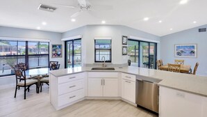 A modern kitchen with white cabinets, a stainless steel dishwasher, and a large window overlooking a body of water. - Pet-friendly Waterfront Home on key lot With View (Marco Island)
