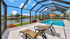 A covered outdoor pool area with lounge chairs and a view of a lake. - Pet-friendly Waterfront Home on key lot With View (Marco Island)