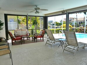 A sunlit room with a ceiling fan, large windows, and a view of a swimming pool and greenery outside. - 1040 Dana Court (Marco Island)