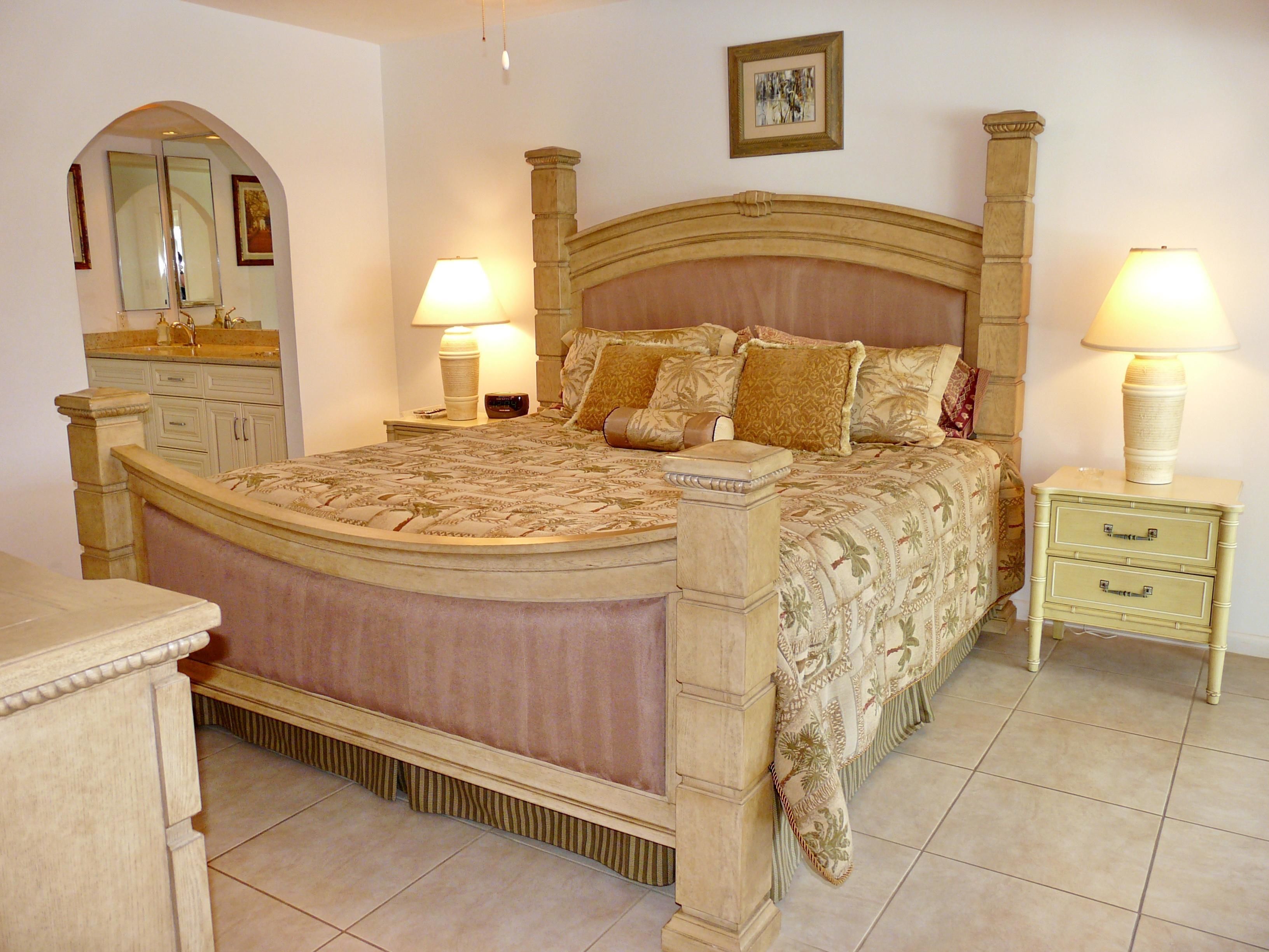 A bedroom with a large bed, two bedside tables with lamps, a dresser, and a mirror.