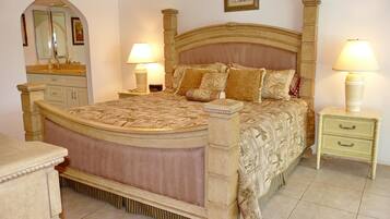 A bedroom with a large bed, two bedside tables with lamps, a dresser, and a mirror.