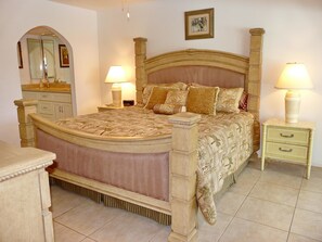 A bedroom with a large bed, two bedside tables with lamps, a dresser, and a mirror. - 1040 Dana Court (Marco Island)