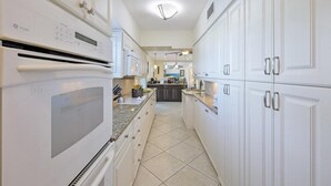 A modern kitchen with white cabinetry, a built-in oven, and a central island. - 775 Willow Court (Marco Island)