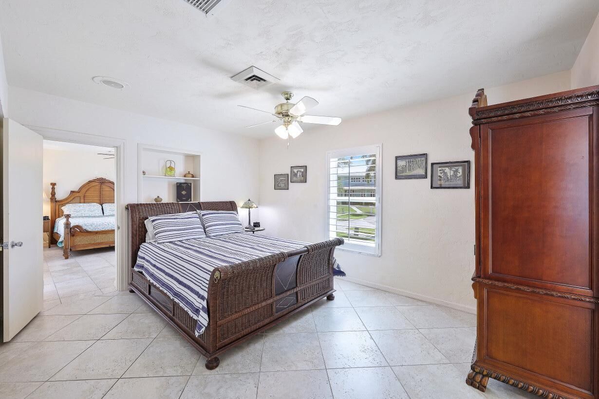 A bedroom with a large bed, a wooden wardrobe, a ceiling fan, and a window with a view.