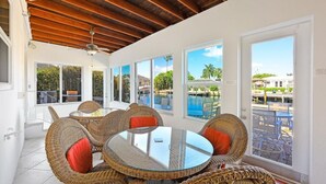 A room with wicker furniture, large windows, and a view of a pool and buildings. - 775 Willow Court (Marco Island)