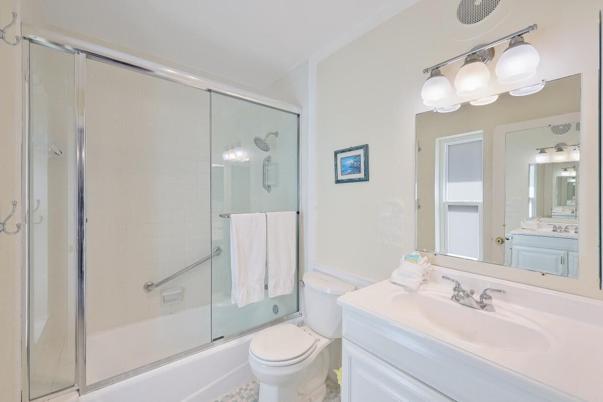 Un baño moderno con ducha de vidrio, inodoro blanco y tocador con un espejo grande.
