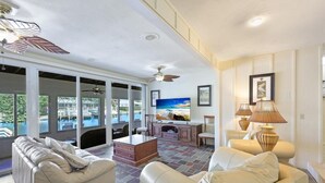 A spacious living area with a large window overlooking a pool, a ceiling fan, and a television. - 775 Willow Court (Marco Island)