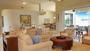 A spacious living room with a high ceiling, a ceiling fan, and a large window offering a view of the outdoors. - 1684 Rainbow Court (Marco Island)