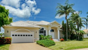 A single-story house with a tiled roof, a garage, and a well-maintained lawn with palm trees. - 1684 Rainbow Court (Marco Island)