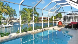 An indoor swimming pool with a glass enclosure, surrounded by palm trees and a view of a marina.