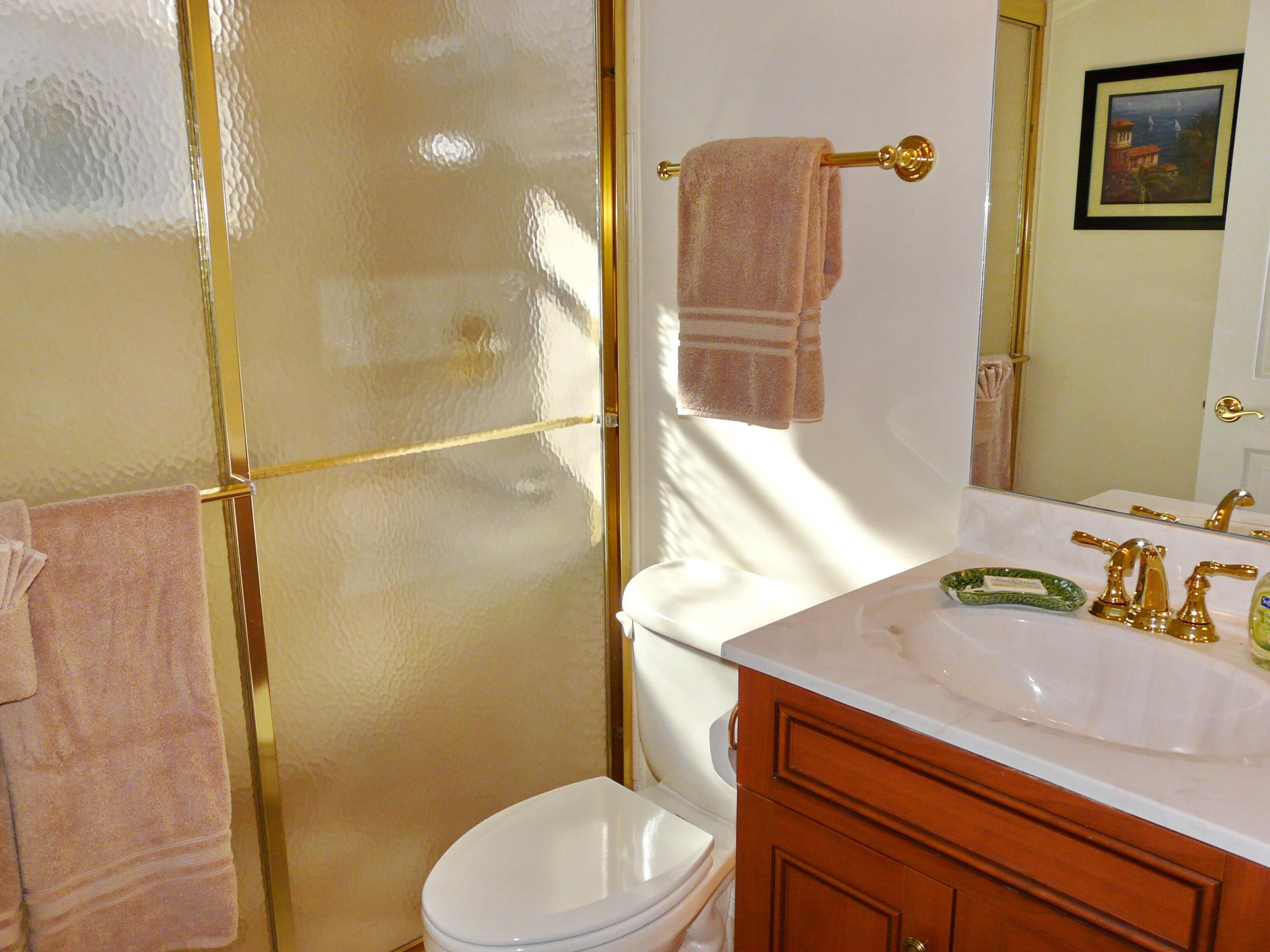 Une salle de bain avec des toilettes blanches, un meuble-lavabo en bois doté d’un robinet doré et une cabine de douche en verre.