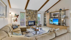En stue med en pejs af natursten, beige sofaer, et sofabord og et fjernsyn på et træskab.