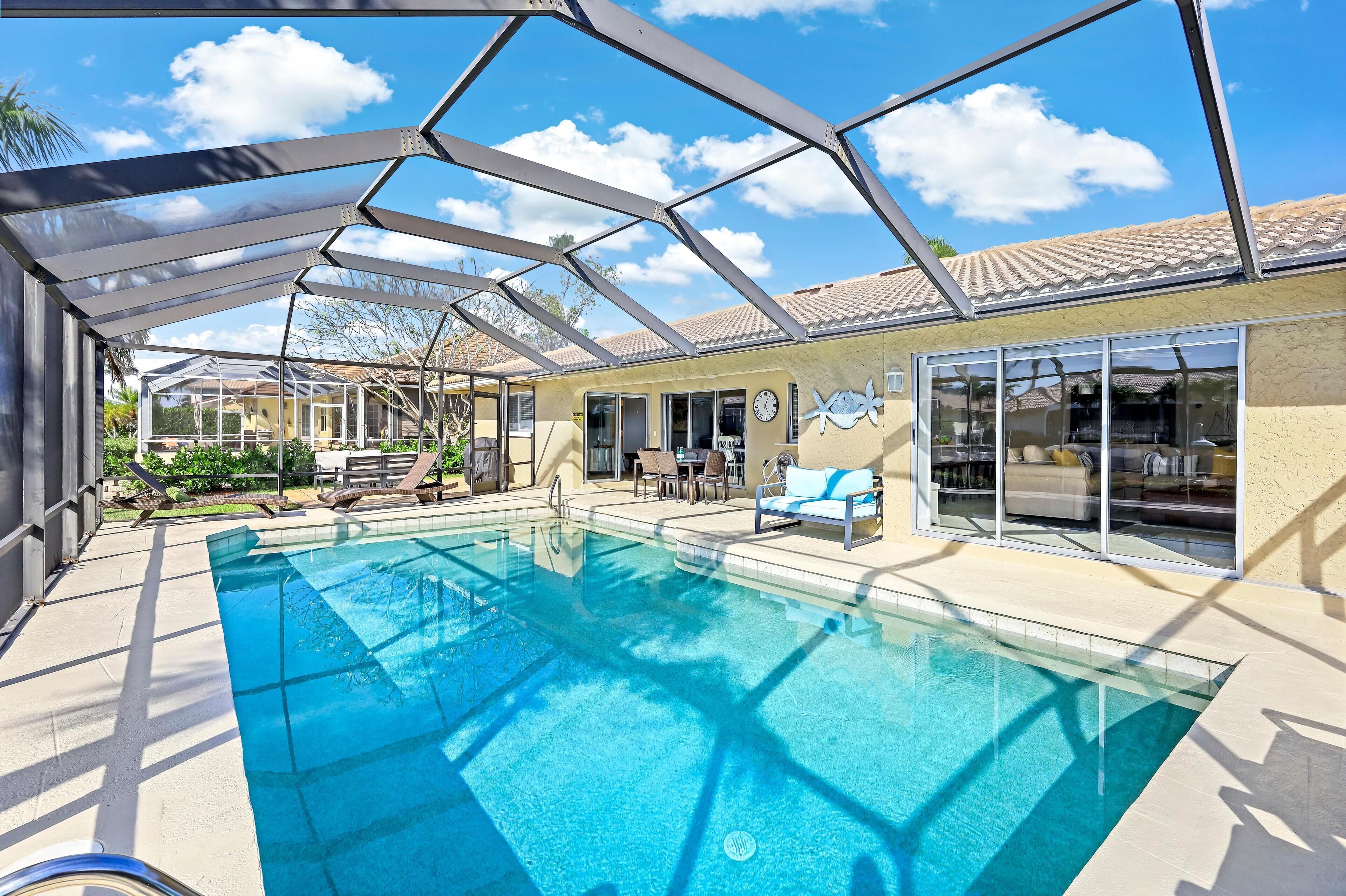 A swimming pool with a glass enclosure, outdoor seating, and a house with large windows.