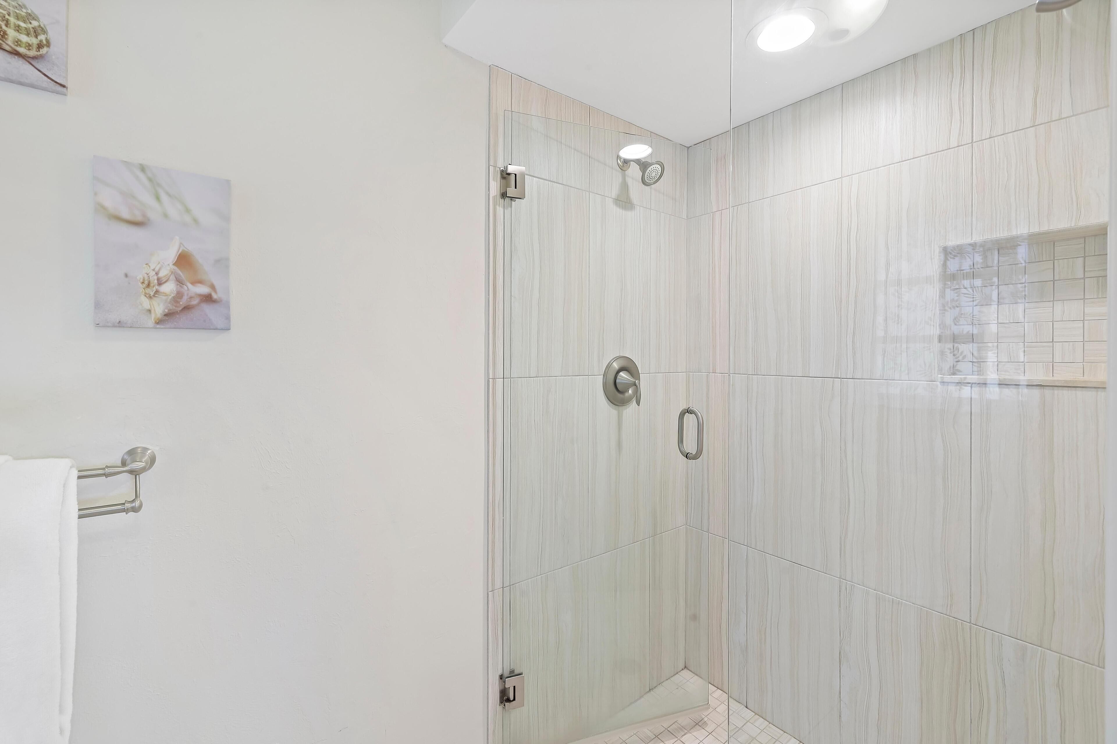 Een moderne badkamer met een douchecabine van glas, witte marmeren tegels en een handdoekhouder.