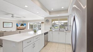 A modern kitchen with white cabinetry, a stainless steel refrigerator, and a large island with a dishwasher. - Waterfront Home With Pool and Western Exposure (Marco Island)
