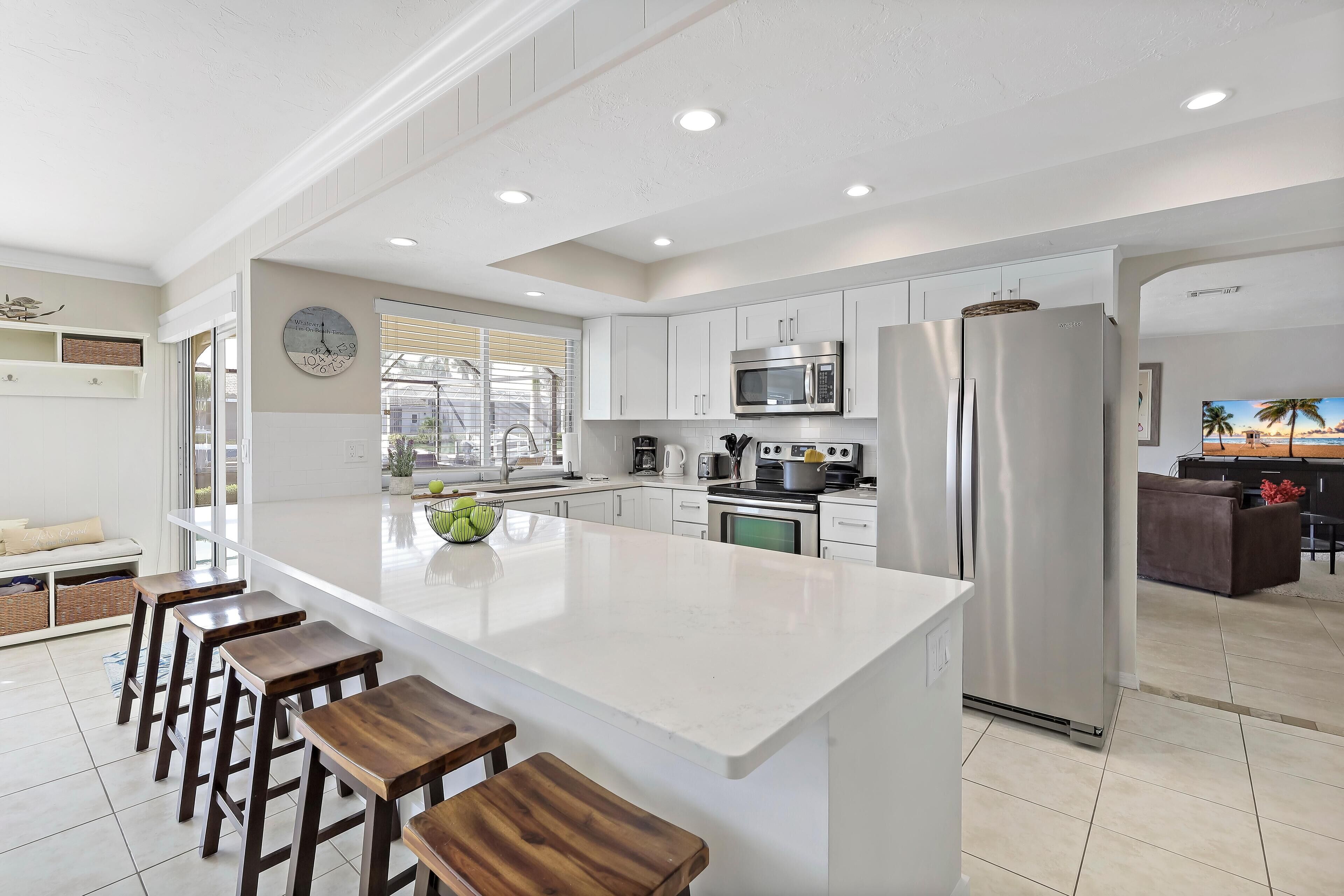 A modern kitchen with white cabinetry, a central island with bar stools, stainless steel appliances, and a large window providing natural light.