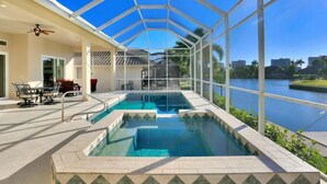 A covered swimming pool with a view of a lake and buildings in the background. - Waterfront Home With Pool, spa and Walk to Beach (Marco Island)