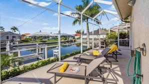 A poolside area with lounge chairs, a view of a water body, and a clear sky. - Waterfront Home With Pool, spa and Walk to Beach (Marco Island)