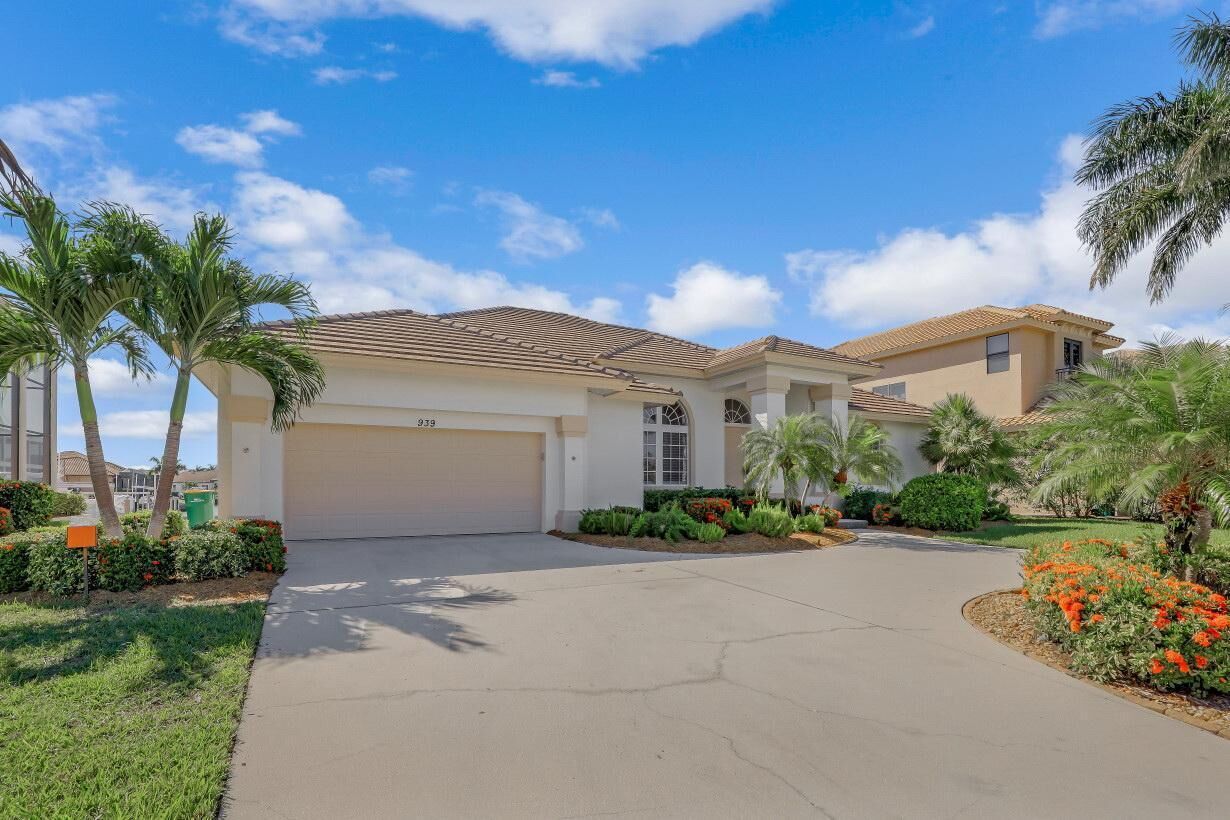 A two-story house with a garage, surrounded by well-maintained landscaping and palm trees.