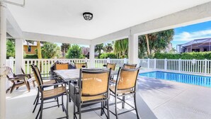 A covered patio with a pool, outdoor furniture, and a white fence. - West-facing Home With Pool and 2nd Floor Porch (Marco Island)