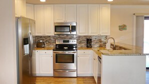 A modern kitchen with stainless steel appliances, white cabinetry, and a herringbone tile backsplash. - West-facing Home With Pool and 2nd Floor Porch (Marco Island)