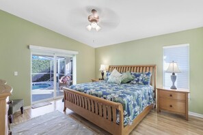 A bedroom with a bed, nightstands, a ceiling fan, and a view of a swimming pool through a sliding glass door. - Pet-friendly Home With Pool and Steps to Beach/food (Marco Island)