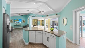 A modern kitchen with white cabinetry, a central island, and a view into the dining area. - Private Home and Guesthouse With Courtyard, Pool and spa (Marco Island)