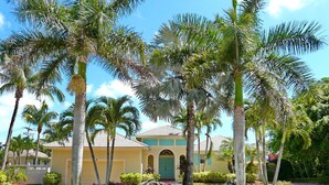A yellow building with a green door, surrounded by palm trees and a well-maintained garden. - Private Home and Guesthouse With Courtyard, Pool and spa (Marco Island)
