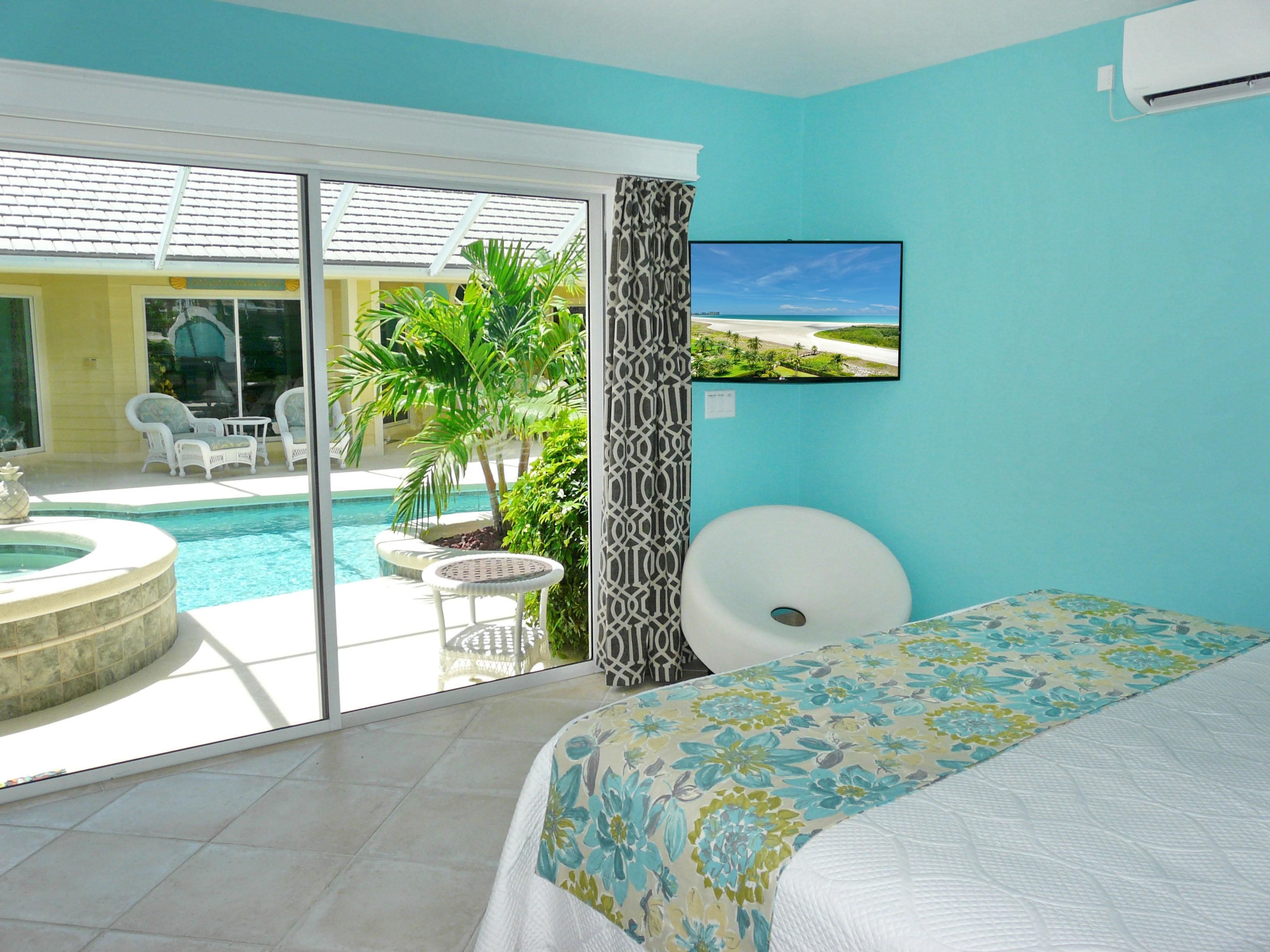 Une chambre d’hôtel comprenant un lit, une télévision, une vue sur la piscine et un espace extérieur avec des chaises et une table.