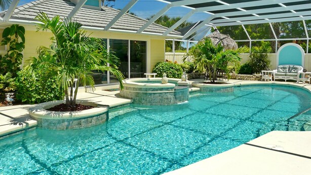 A pool area with a glass-enclosed structure, a hot tub, and various plants. - Private Home and Guesthouse With Courtyard, Pool and spa (Marco Island)
