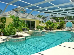 A pool area with a glass-enclosed structure, a hot tub, and various plants. - Private Home and Guesthouse With Courtyard, Pool and spa (Marco Island)