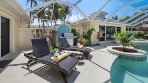 A covered outdoor area with lounge chairs, a barbecue grill, and a pool. - Private Home and Guesthouse With Courtyard, Pool and spa (Marco Island)