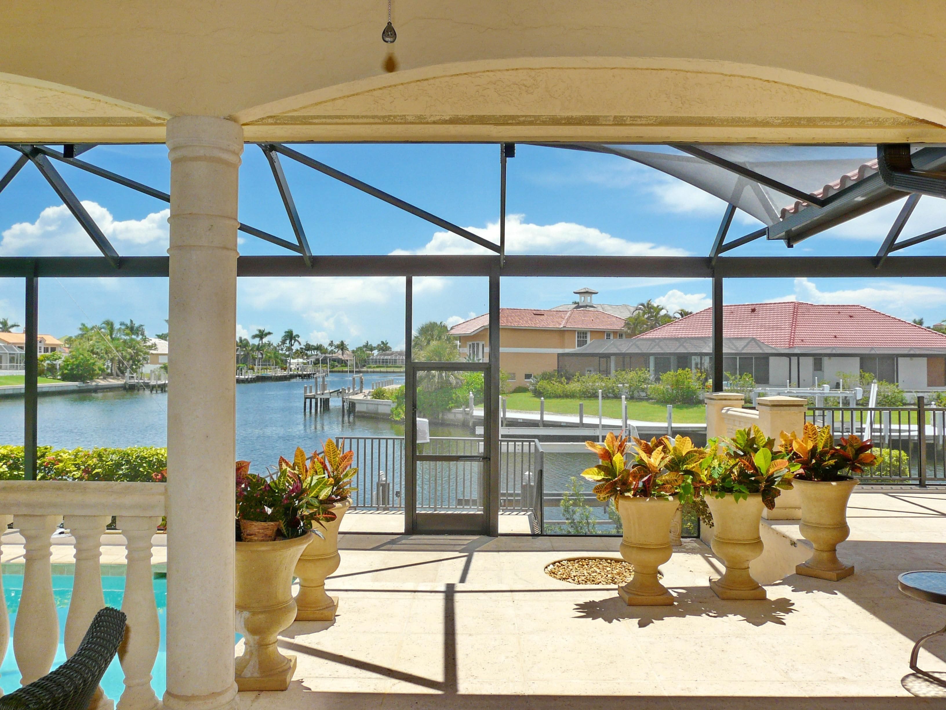 A covered outdoor area with large windows overlooking a body of water and a residential area.