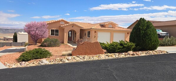 A single-story house with a beige exterior, a garage, and a landscaped front yard with a rock garden and a tree.