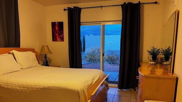 A hotel room with a bed, a nightstand, a lamp, a dresser, and a view of the outdoors. - Exceptional Lake Powell View Home, lots of parking! (Page)