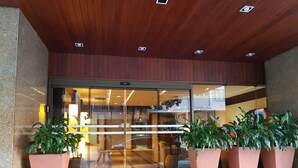 Entrada de hotel con puerta de vidrio, plantas en macetas y suelo de baldosas.