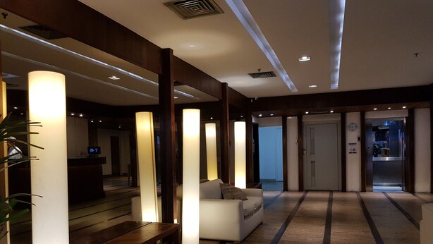 Un moderno vestíbulo de hotel con una recepción, una zona de estar con sofá y una escalera que sube a un piso superior.