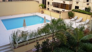 Una piscina en la azotea con sillones de descanso y plantas en macetas.