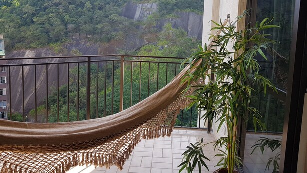 Un balcón con una hamaca, plantas de bambú y vistas a un paisaje montañoso.