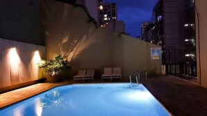 Piscina con sillones de descanso y una planta en maceta, rodeada por una terraza de madera y un muro bajo.