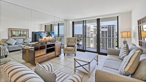 A modern living room with a sofa, armchair, TV, and a coffee table. - Sun-bright Beachfront Condo With Pool/tennis Courts (Marco Island)