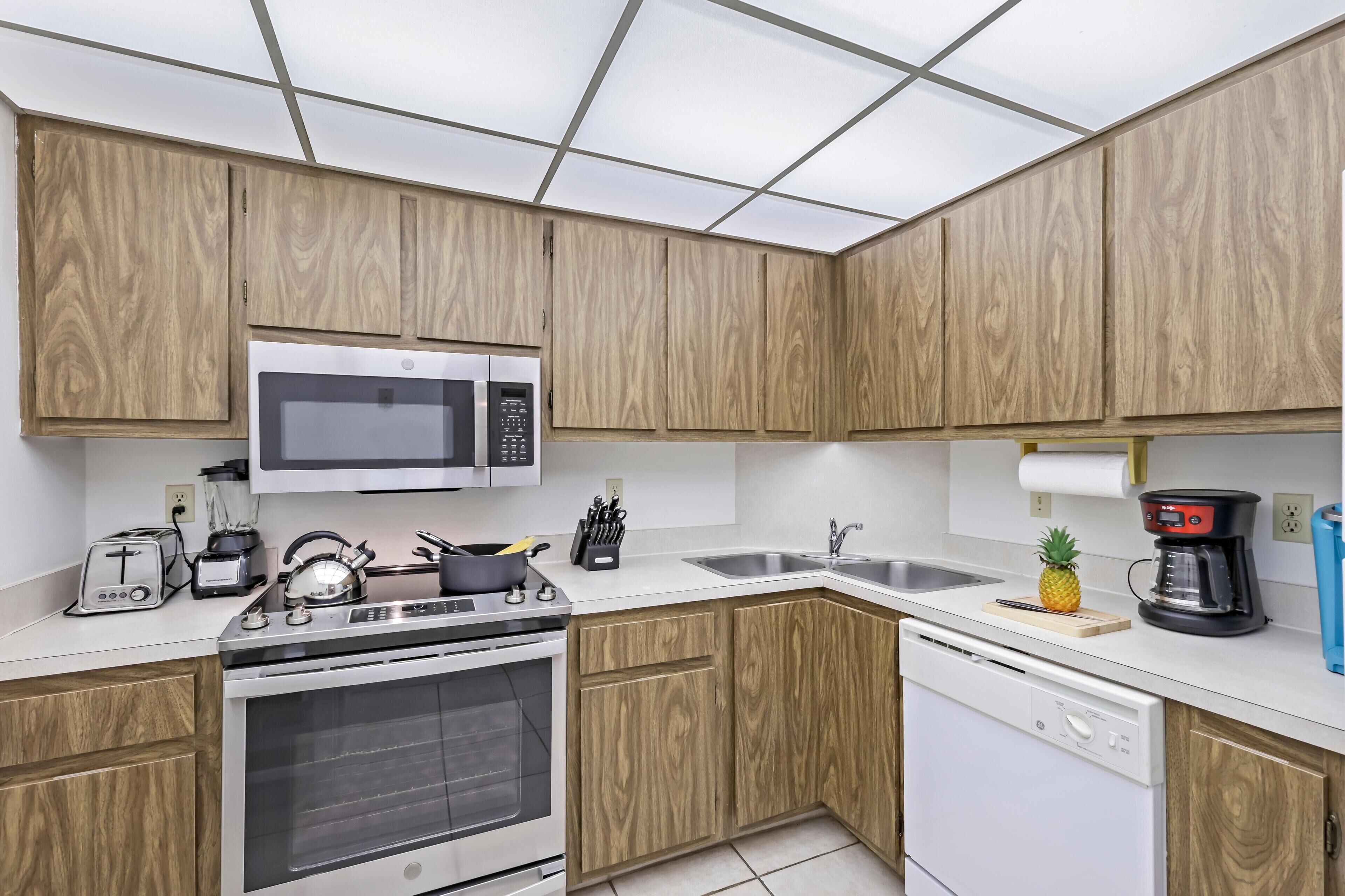A modern kitchen with wooden cabinets, stainless steel appliances, and a white countertop.