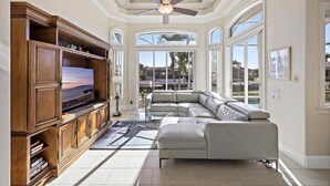A spacious living room with a large sectional sofa, a wooden entertainment unit, and a ceiling fan. - Pet-friendly Waterfront Home With Heated Pool and spa (Marco Island)